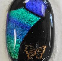 oval black glass with glittering turquoise and blue shapes, a bronze butterfly appears in the bottom right